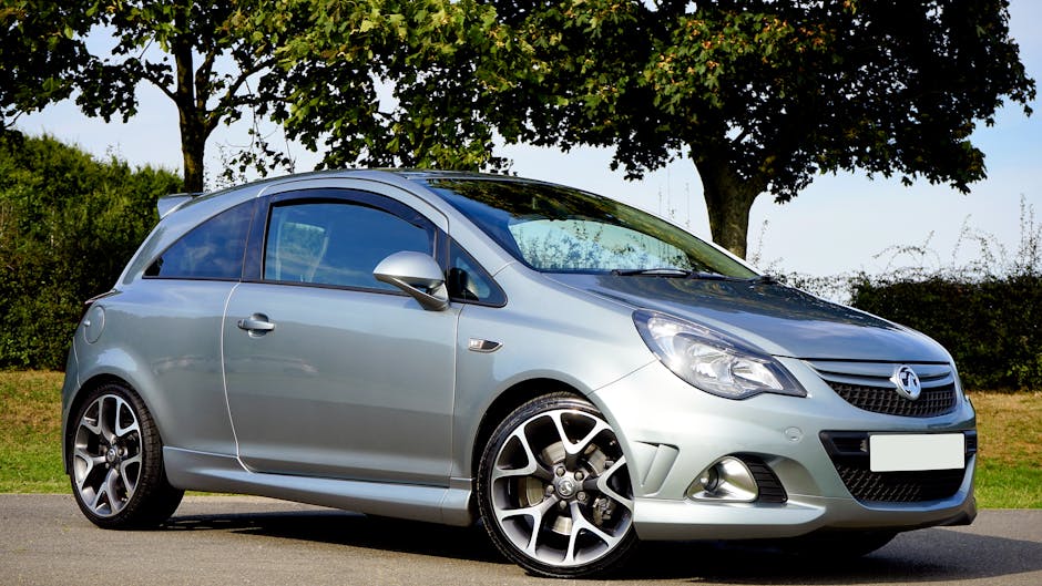 Silver hatchback car parked on a sunny day with trees in the background.